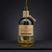 Vibrant golden Navarino Icons extra virgin olive oil being poured into a glass bowl against a dark, minimalist professional studio background.