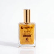 Shimmering Golden Elixir by Mastic Spa, hydrated and glow, 100ml bottle with gold cap on a reflective surface against a dark background.