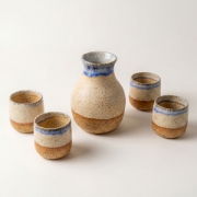 Handmade ceramic carafe and 4 shot glasses set with dual-tone blue and sandy glaze on white background.
